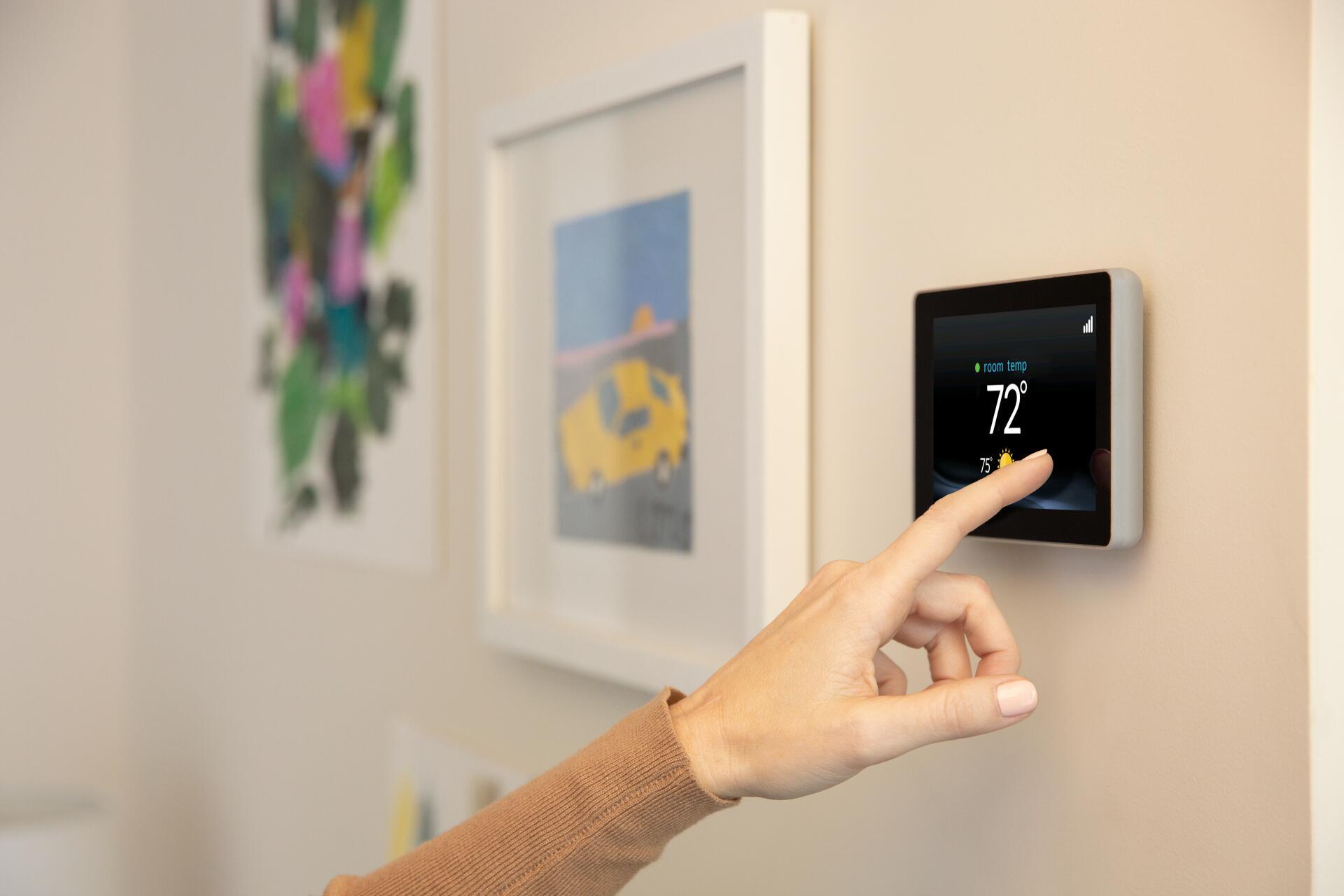 Image of a hand adjusting the heat in their home on a digital screen thermostat.