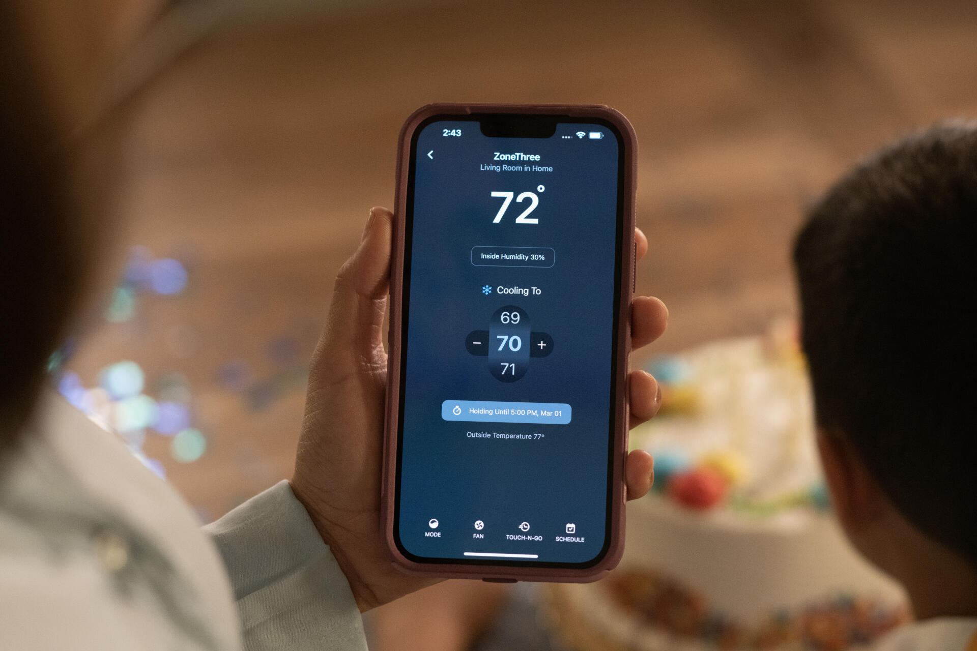 Image of a homeowner holding a phone with air conditioning controls in an app. Hometown Heating can help improve your homes indoor air quality.